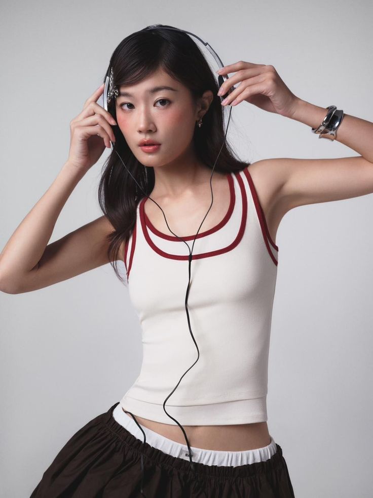 Woman in a tank top and skirt holding headphones against a white background