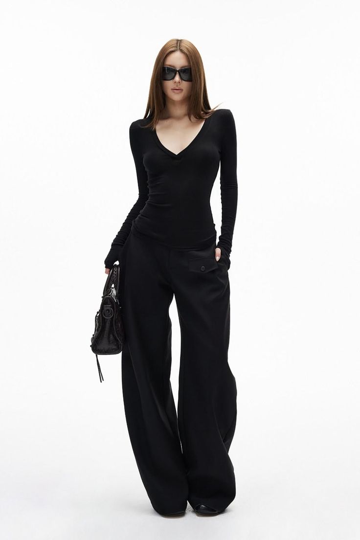 Woman in black long-sleeve top, wide-leg pants, and sunglasses holding a handbag