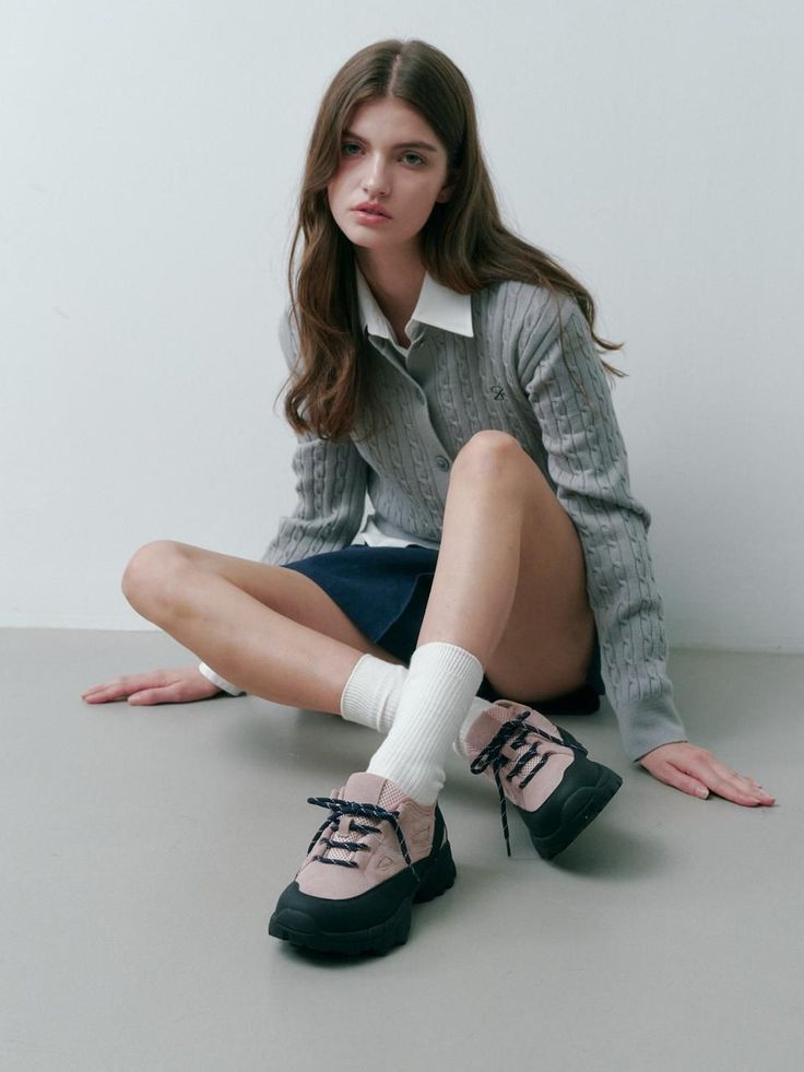 Woman with long hair wearing a cable knit cardigan and mini skirt, sitting indoors