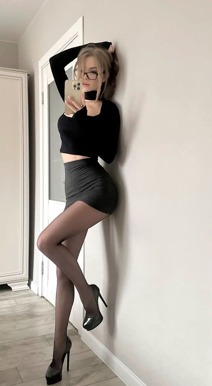 Woman in a black top and mini skirt posing for a mirror selfie