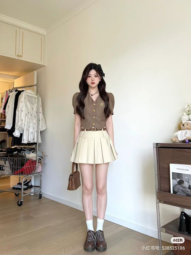 Woman in a brown top and pleated skirt standing indoors