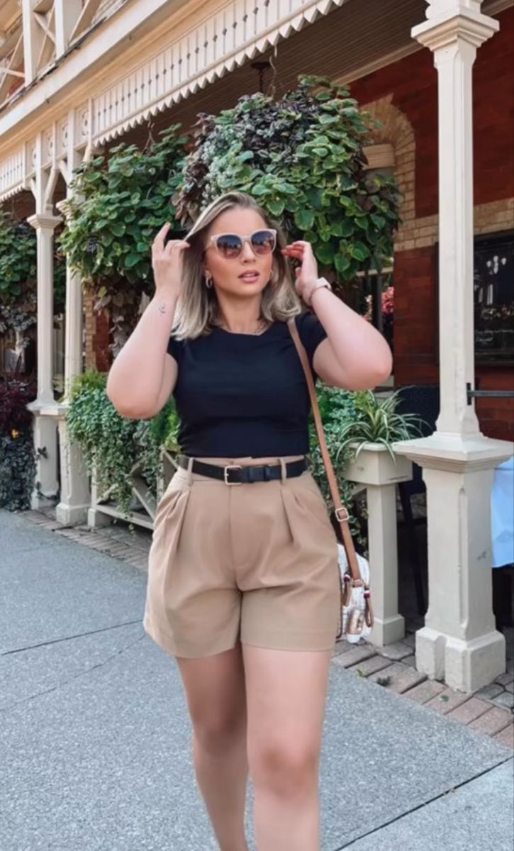 Woman with blonde hair and sunglasses wearing a black t-shirt and khaki shorts outdoors