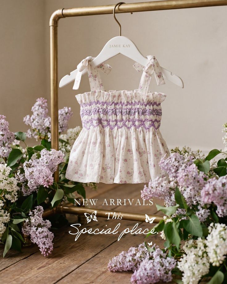 Baby top with floral print and smocking, surrounded by lilac flowers