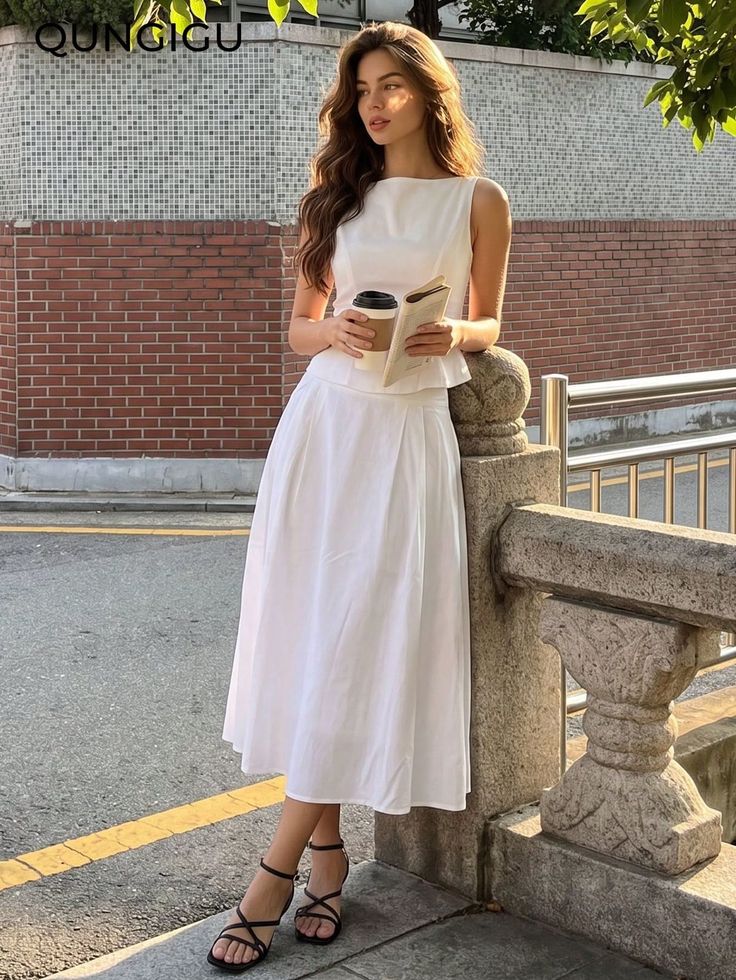 Woman in a white dress holding a coffee cup and book outdoors