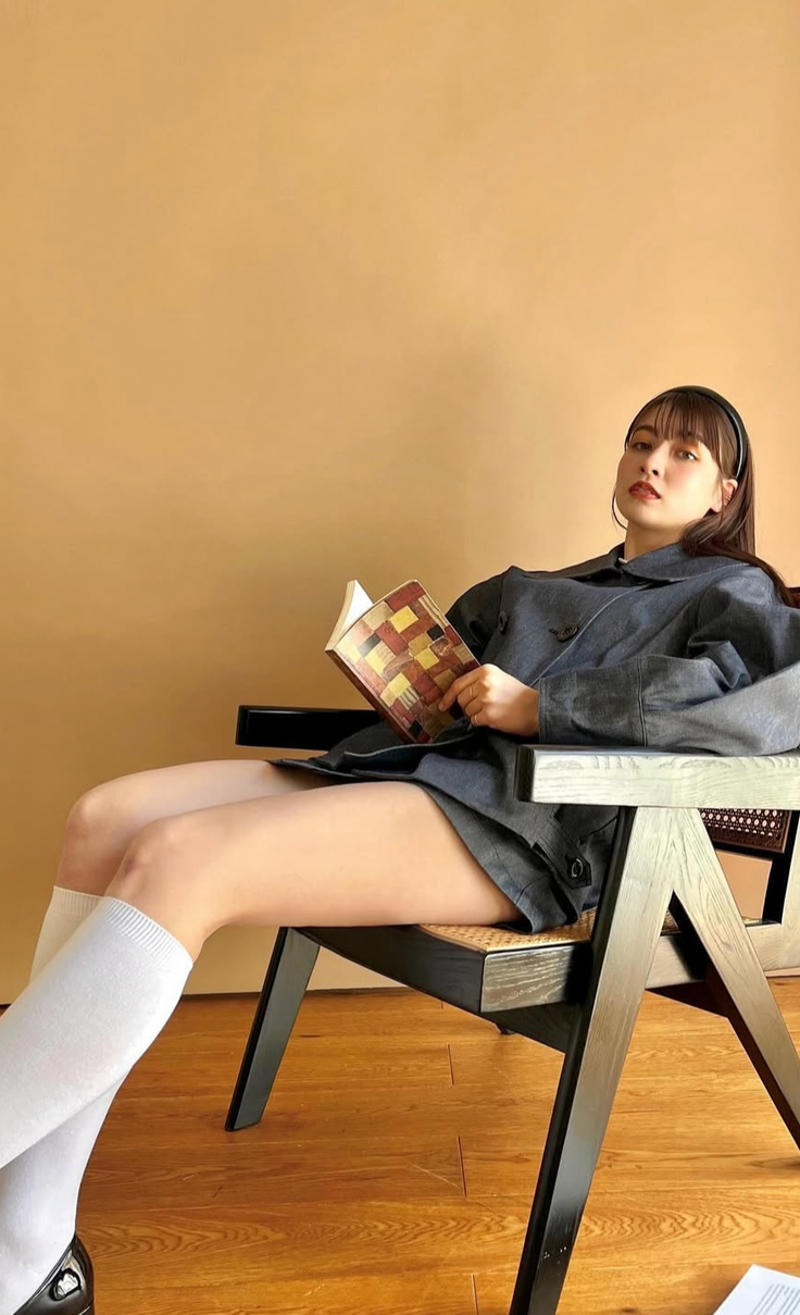 Woman in a denim jacket and white socks sitting in a chair reading a book