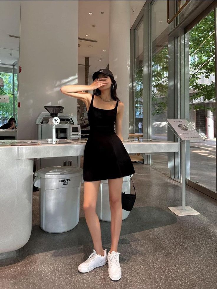 Woman in a black dress and baseball cap covering her face indoors