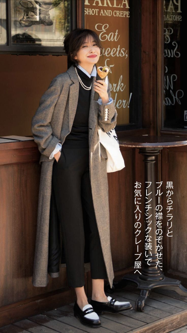 Woman in a long plaid coat and black pants holding a crepe outdoors
