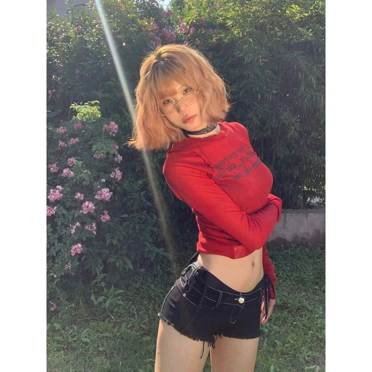 Woman with short hair and glasses in a red top and black shorts outdoors