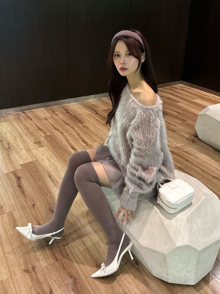 Woman in an off-shoulder sweater and thigh-high socks sitting indoors