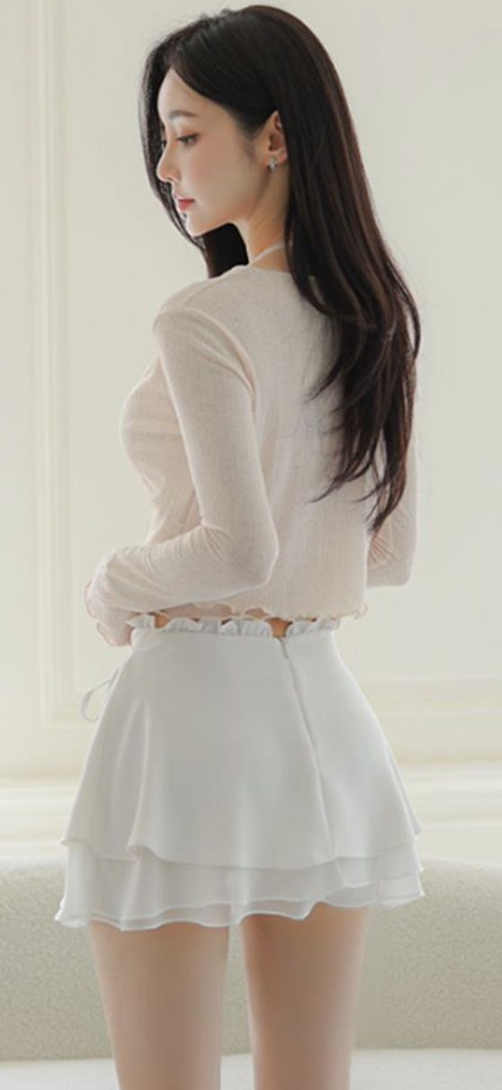 Woman with long dark hair wearing a light top and white ruffled skirt indoors