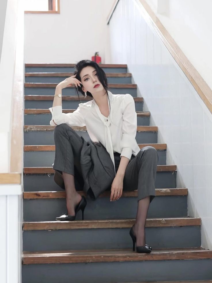 Woman in a white shirt and suit pants sitting on wooden stairs
