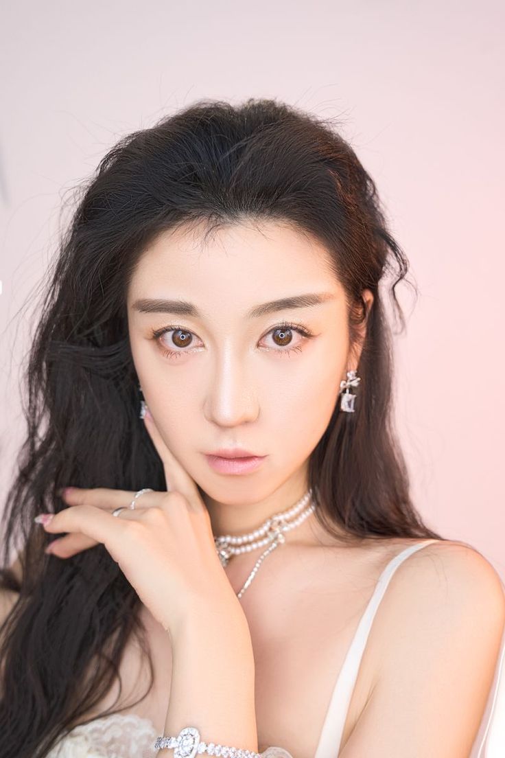 Woman with long dark hair and jewelry against a pink background