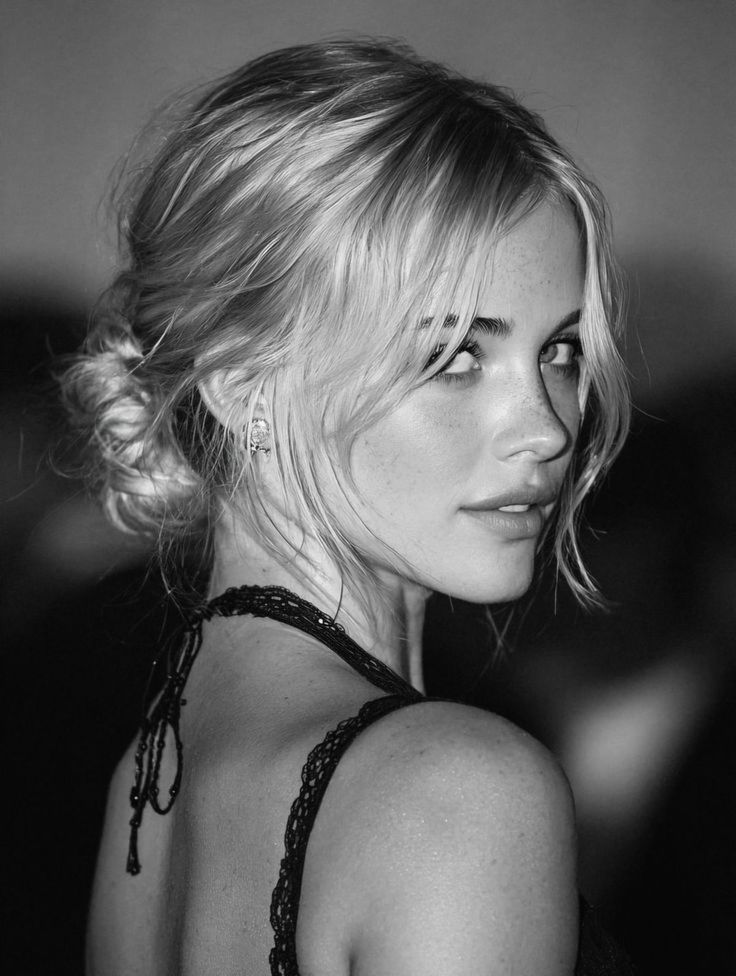 Woman with blonde hair in an updo wearing a lace top, looking over her shoulder