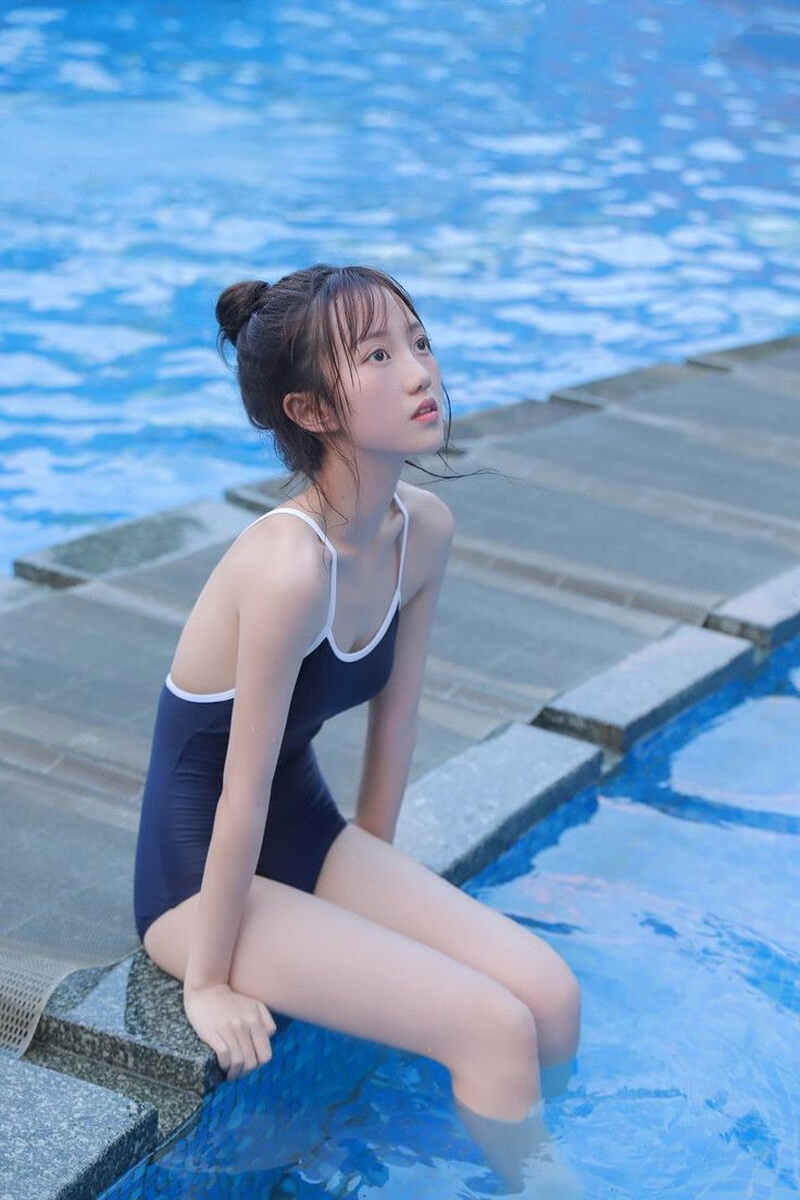 Young woman in a dark blue swimsuit sitting by a swimming pool