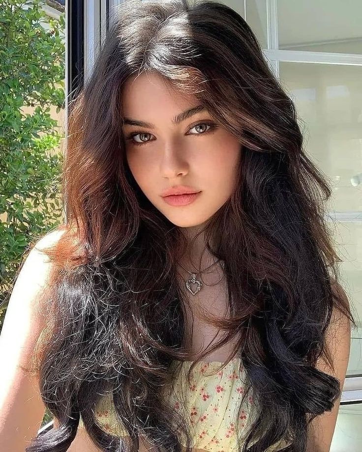 Woman with long dark hair wearing a heart necklace and floral top outdoors