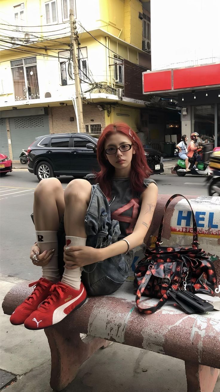 Person with red hair and glasses sitting on a bench on a street