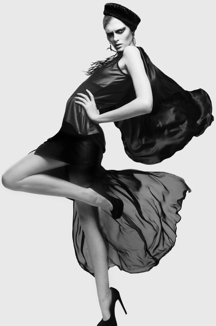 Woman in a black dress and hat posing dramatically in a studio