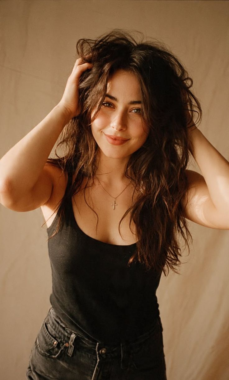Woman with long messy hair in a black tank top and cross necklace