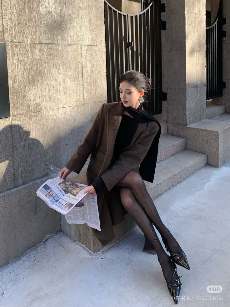 Woman in a brown coat and black tights sitting outdoors, reading a newspaper