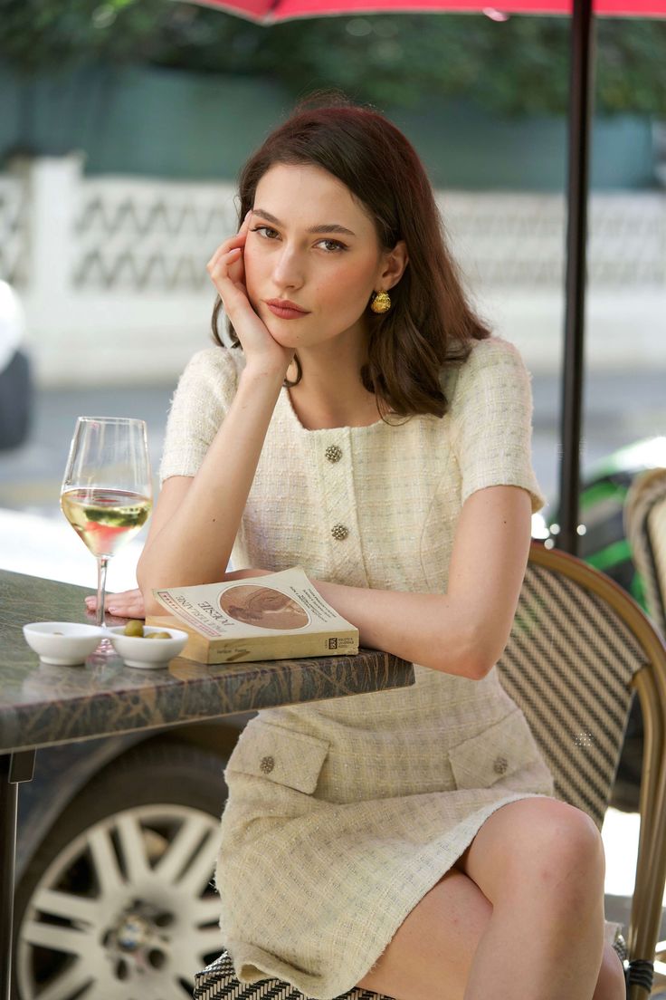 Woman in a tweed dress sitting at an outdoor cafe with a book and wine