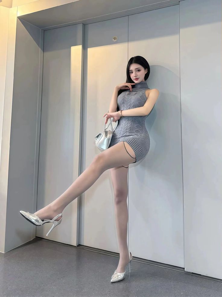 Woman in a gray knit dress and silver heels posing indoors
