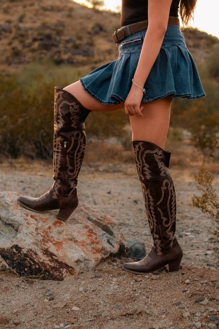 Woman in a denim skirt and cowboy boots posing in a desert landscape