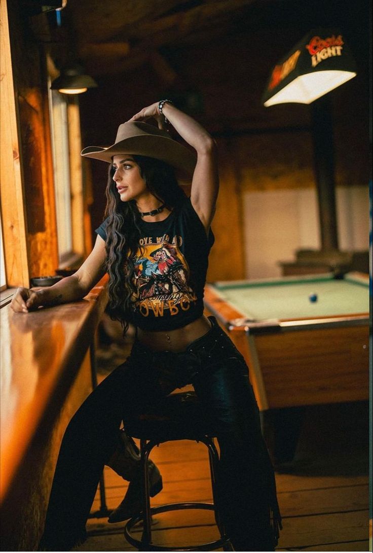 Woman in a cowboy hat and crop top posing in a bar with a pool table