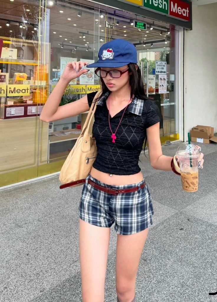 Woman in a crop top and plaid shorts holding iced coffee outdoors
