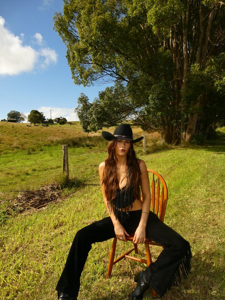 Woman in a cowboy hat and fringe top sitting on a chair in a grassy field
