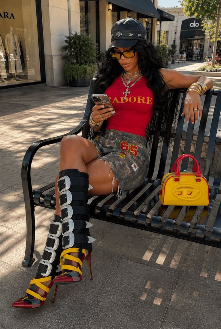 Woman with long hair wearing a red top and camouflage shorts, sitting on a bench outdoors