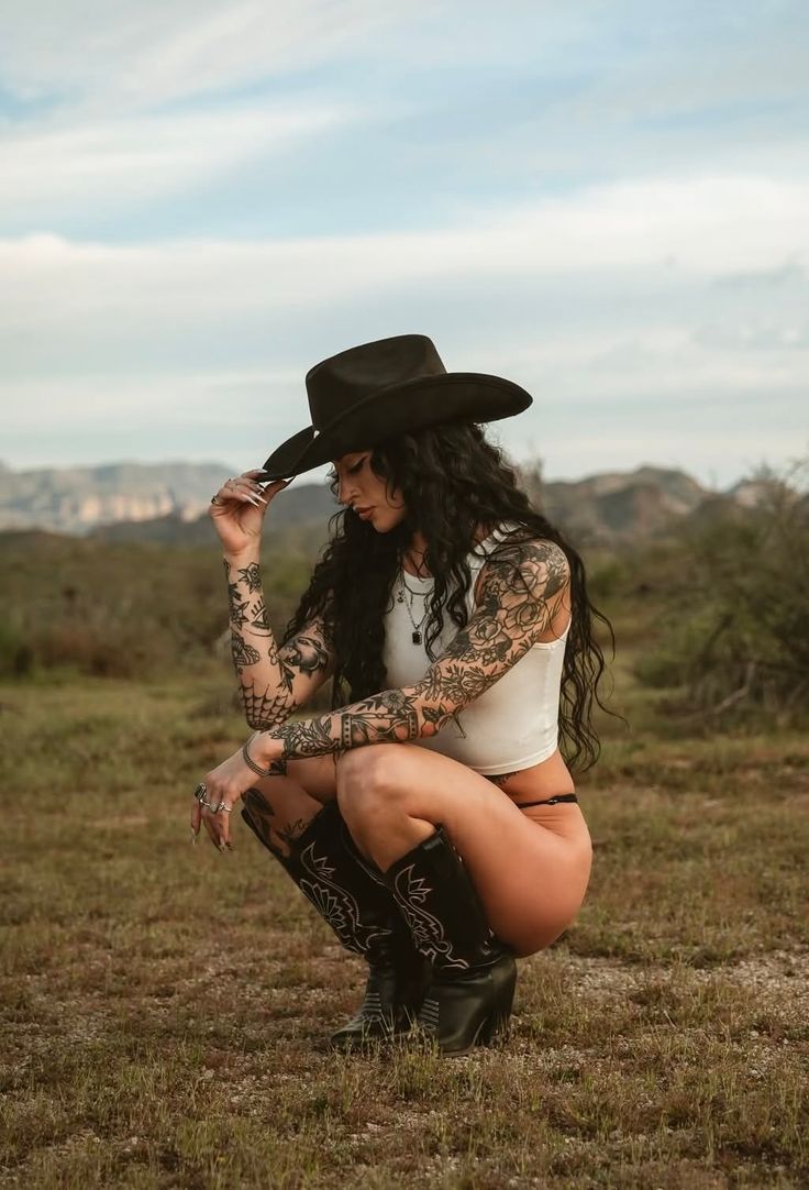 Woman in a cowboy hat and boots squatting in a desert landscape