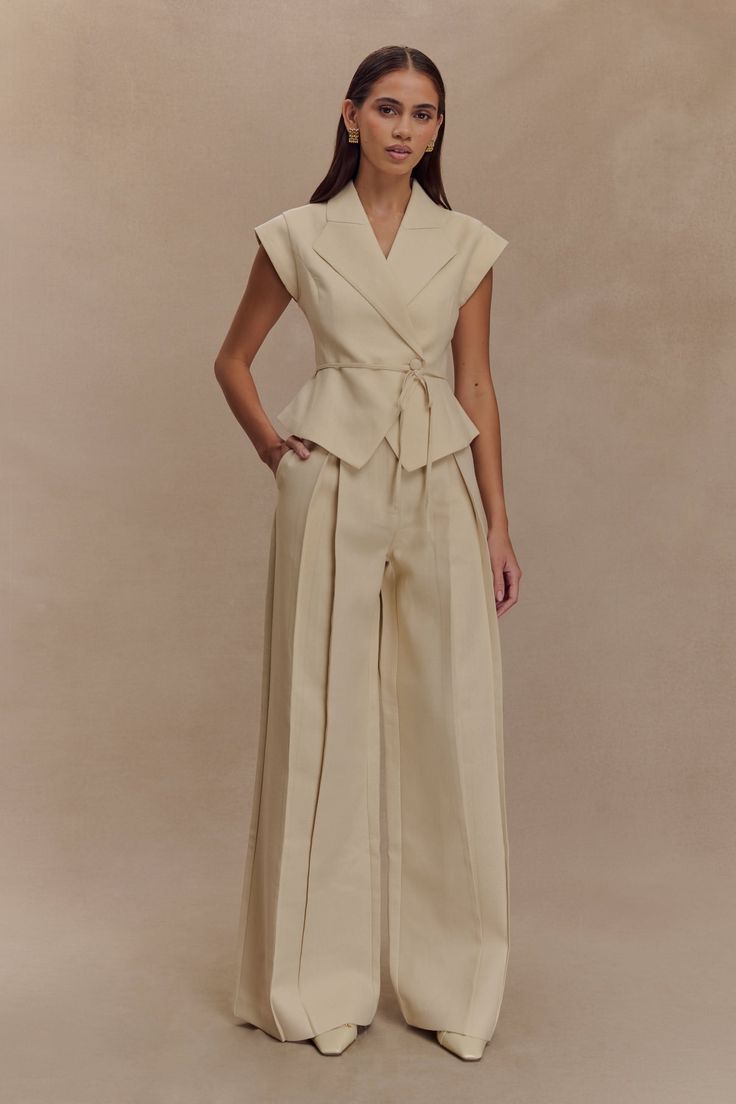 Woman in a beige peplum top and wide leg pants posing in a studio