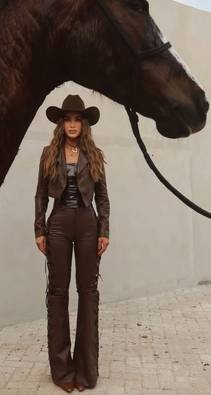 Woman in a brown cowboy hat and leather outfit standing next to a horse