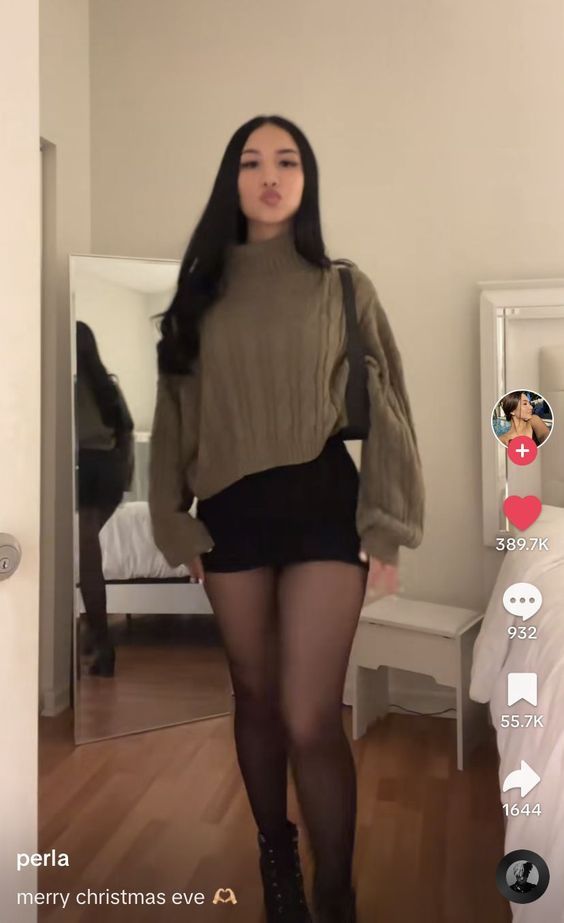 Woman in a turtleneck sweater, mini skirt, and tights posing indoors