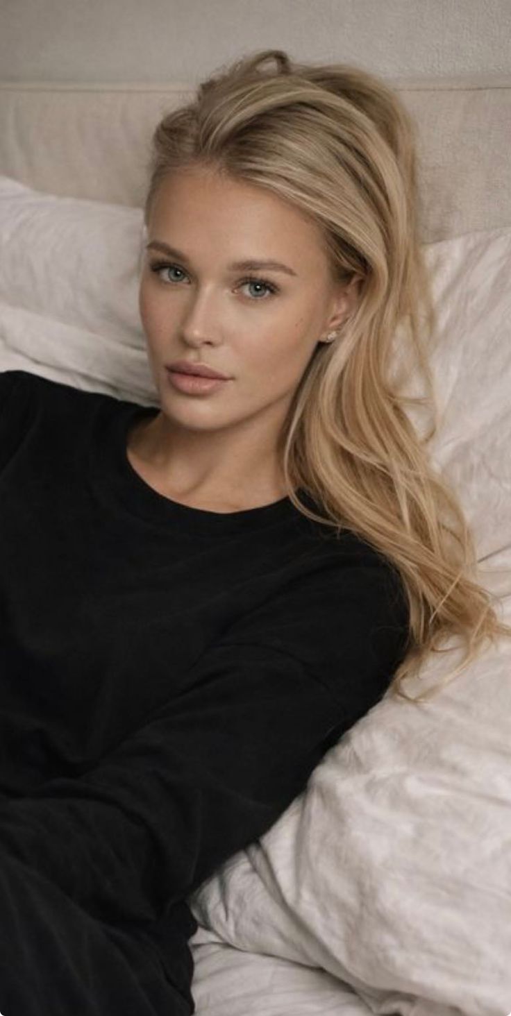 Woman with blonde hair and blue eyes wearing a black shirt, lying in bed