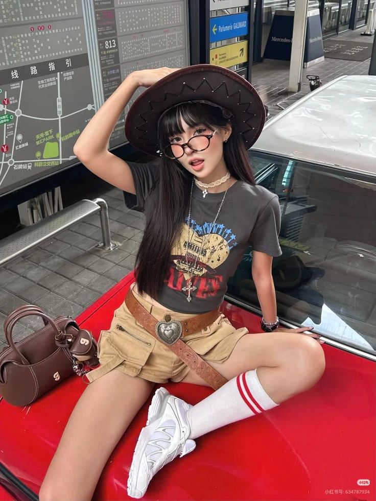 Woman in a cowboy hat and crop top sitting on a red car