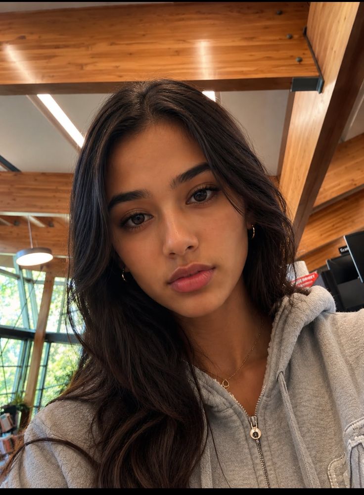 Woman with long dark hair wearing a grey hoodie and necklace indoors