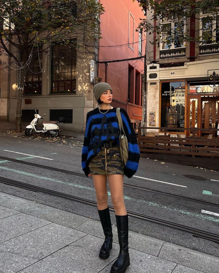 Woman in a beanie, striped sweater, and camo skirt on a city street
