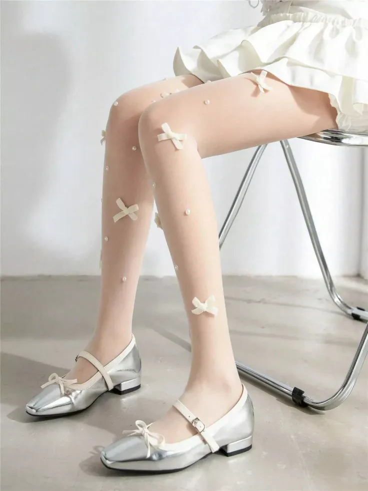 Person wearing white tights with bows and pearls, silver mary jane shoes, and a white dress