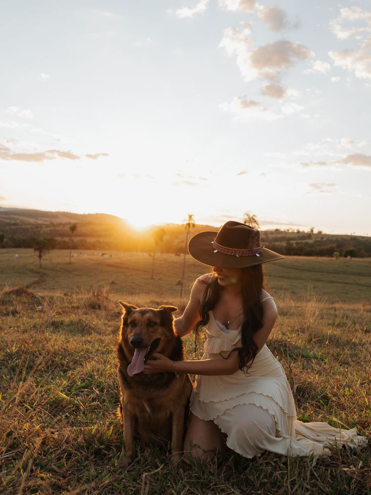 Woman in a cowboy hat with a dog in a field at sunset