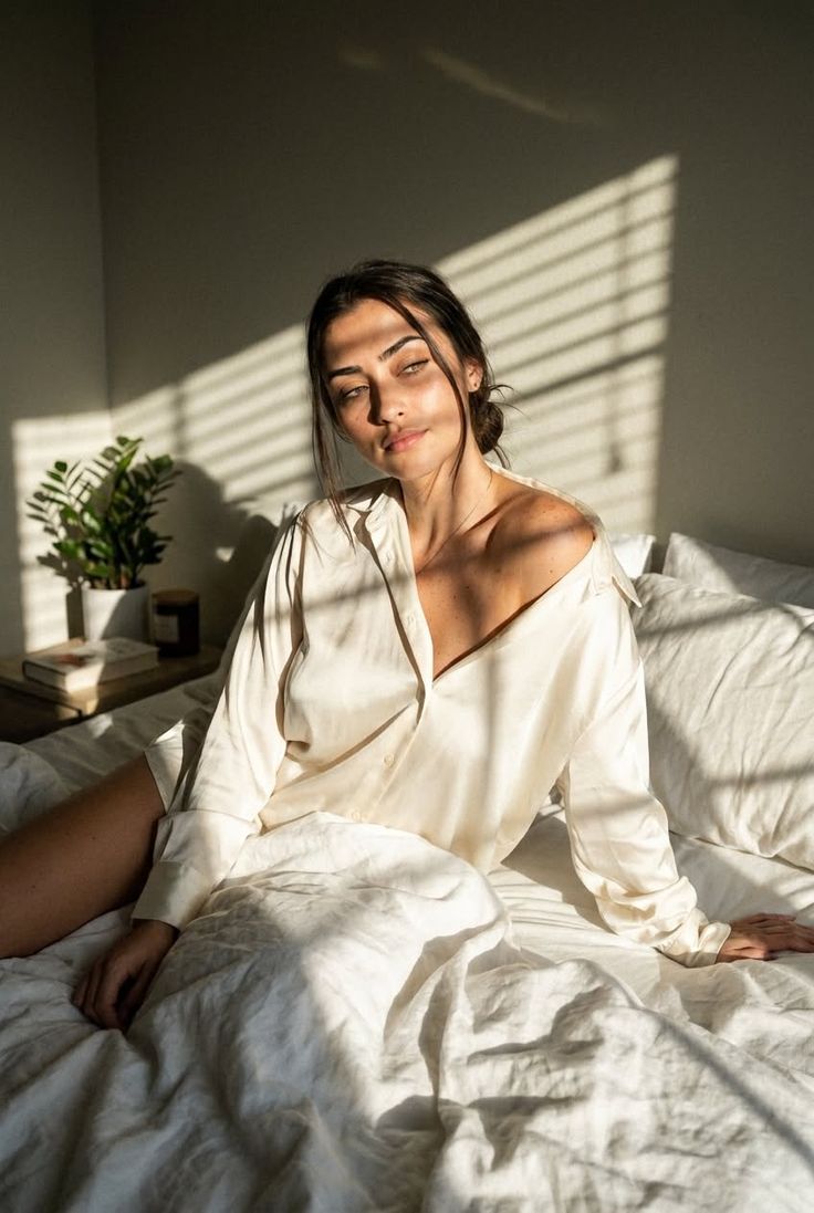 Woman in a white shirt sitting on a bed with natural light and shadows