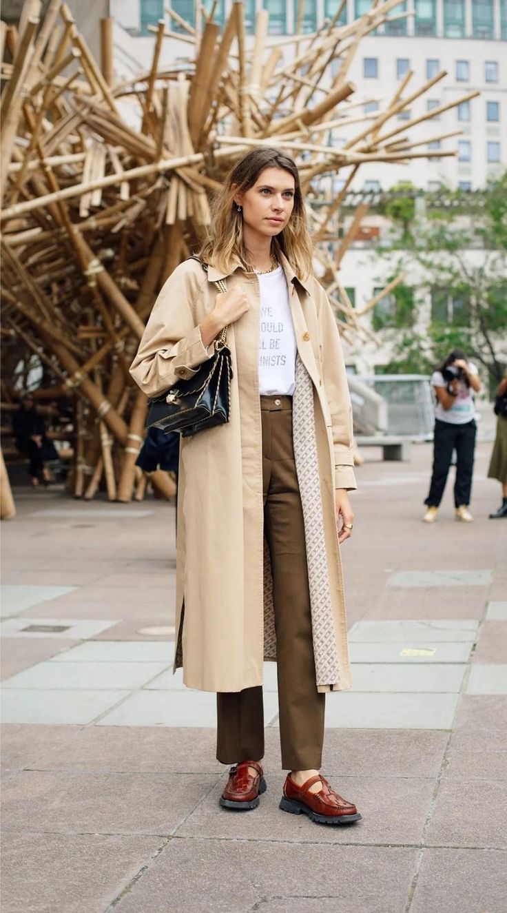 Woman in a trench coat and brown pants standing outdoors