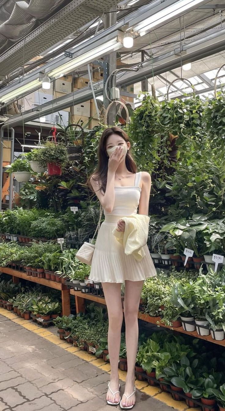 Woman in a white top and pleated skirt with a face mask in a plant nursery