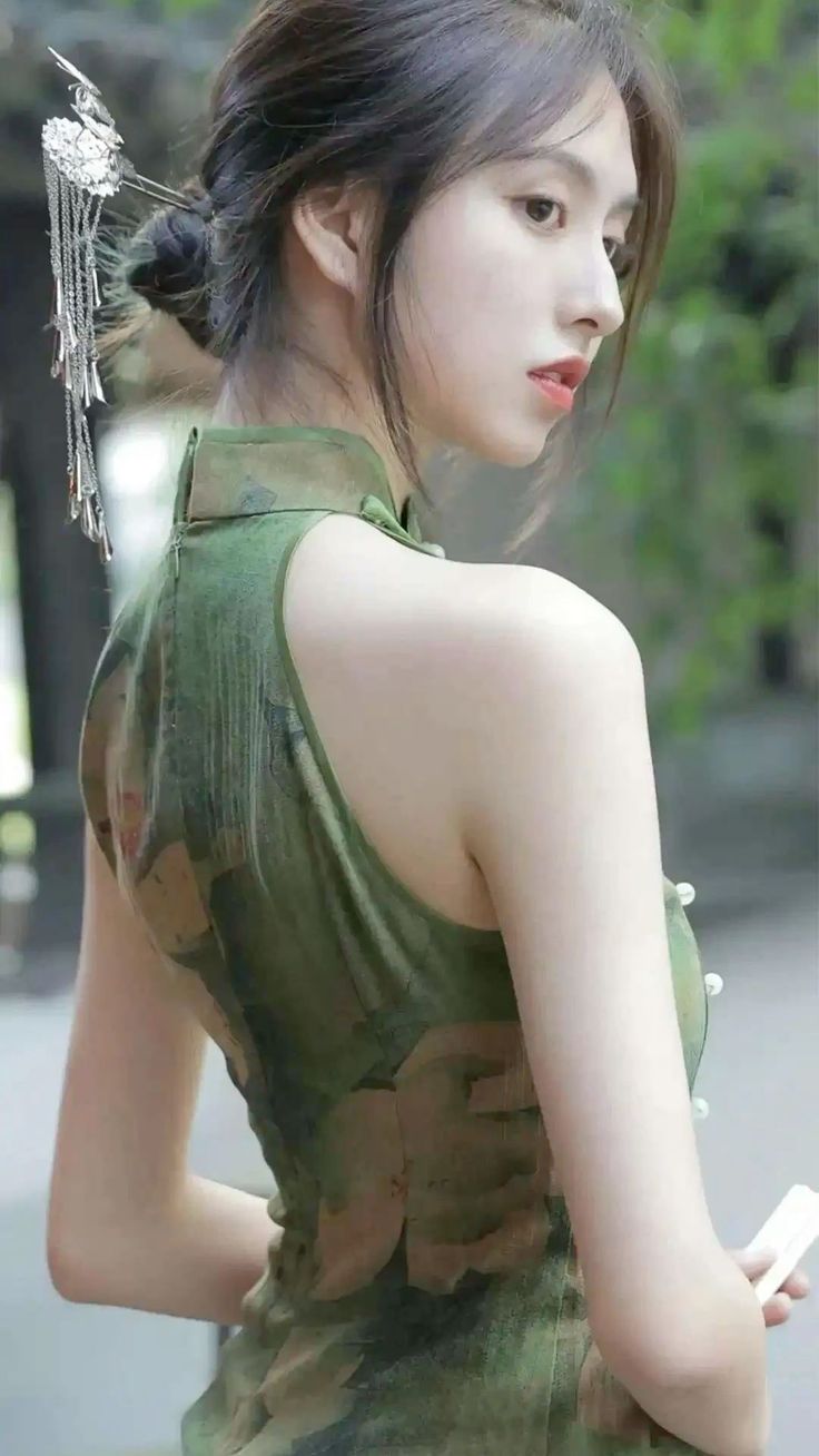 Woman in a green cheongsam with a decorative hair ornament looking over her shoulder