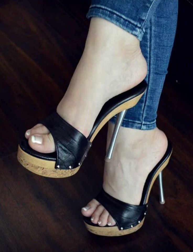 Person wearing black high heels and blue jeans on a wooden floor