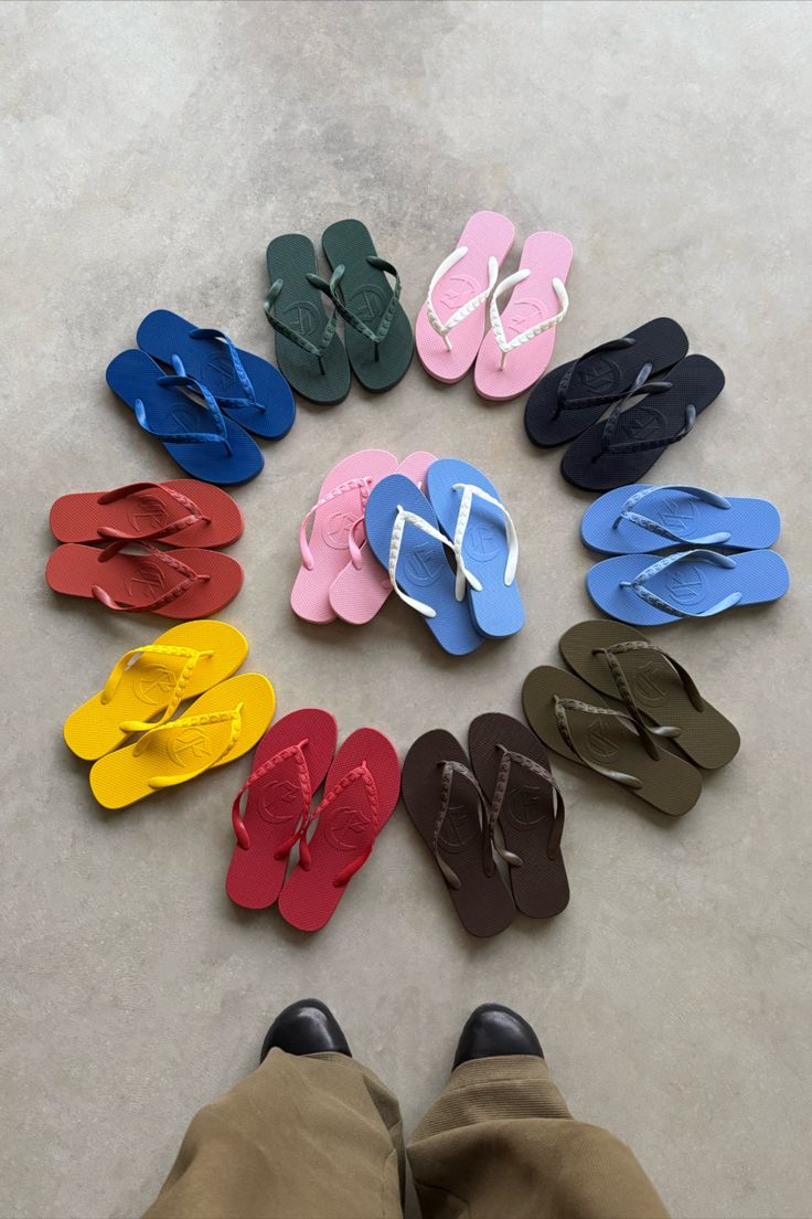 Multiple pairs of colorful flip flops arranged in a circle on a concrete floor