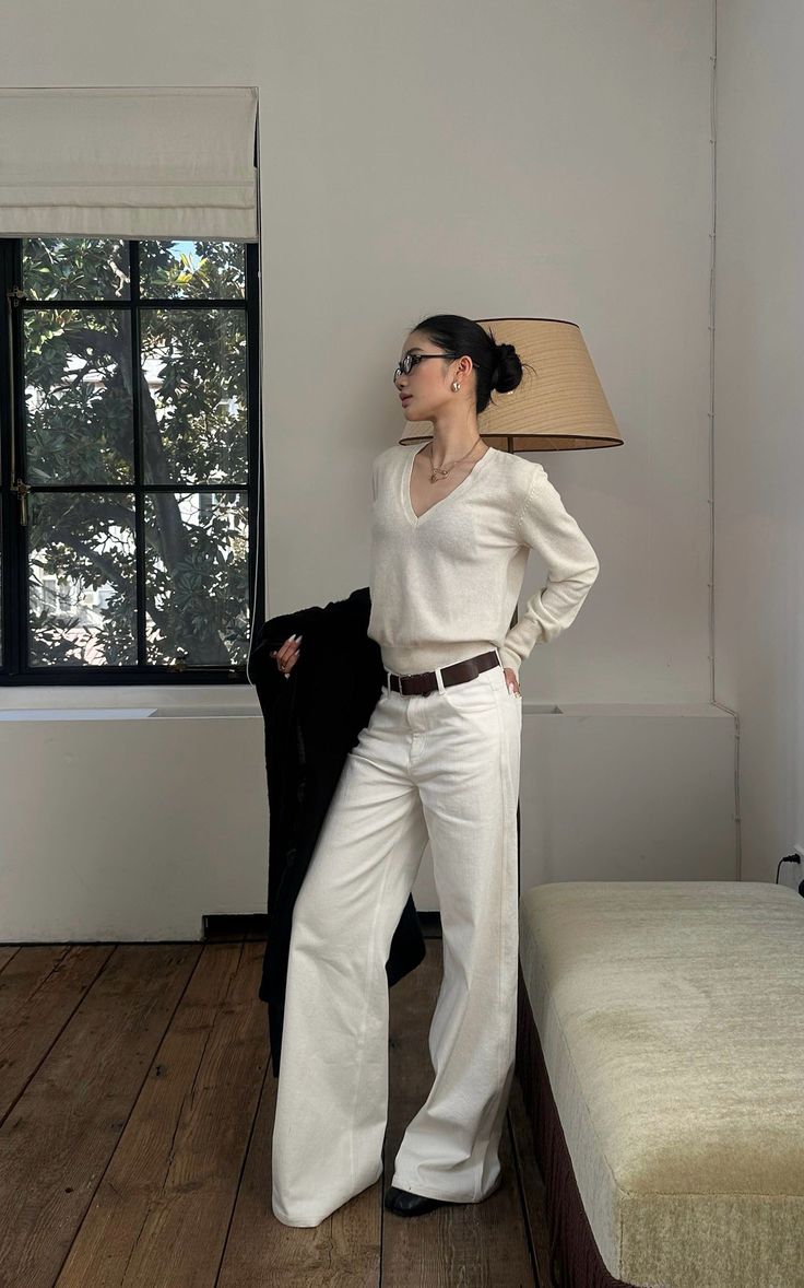 Woman in a white v-neck sweater and white pants with a brown belt indoors