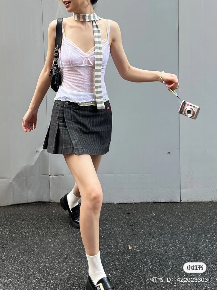Person in a sheer camisole and mini skirt holding a digital camera outdoors