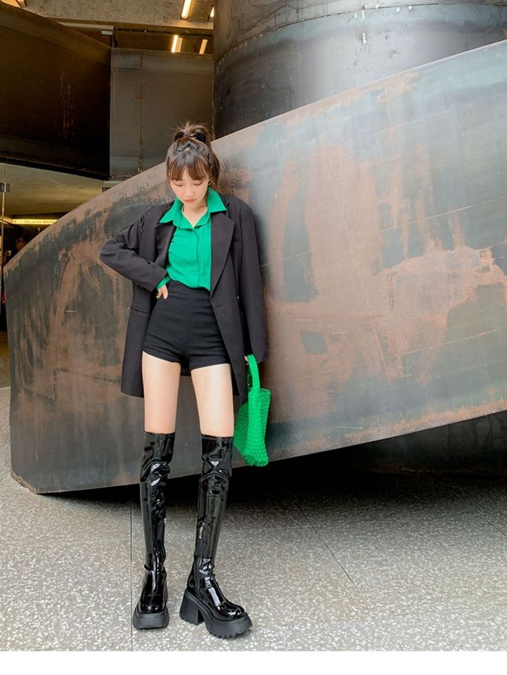 Woman in a black blazer, green shirt, and thigh high boots indoors