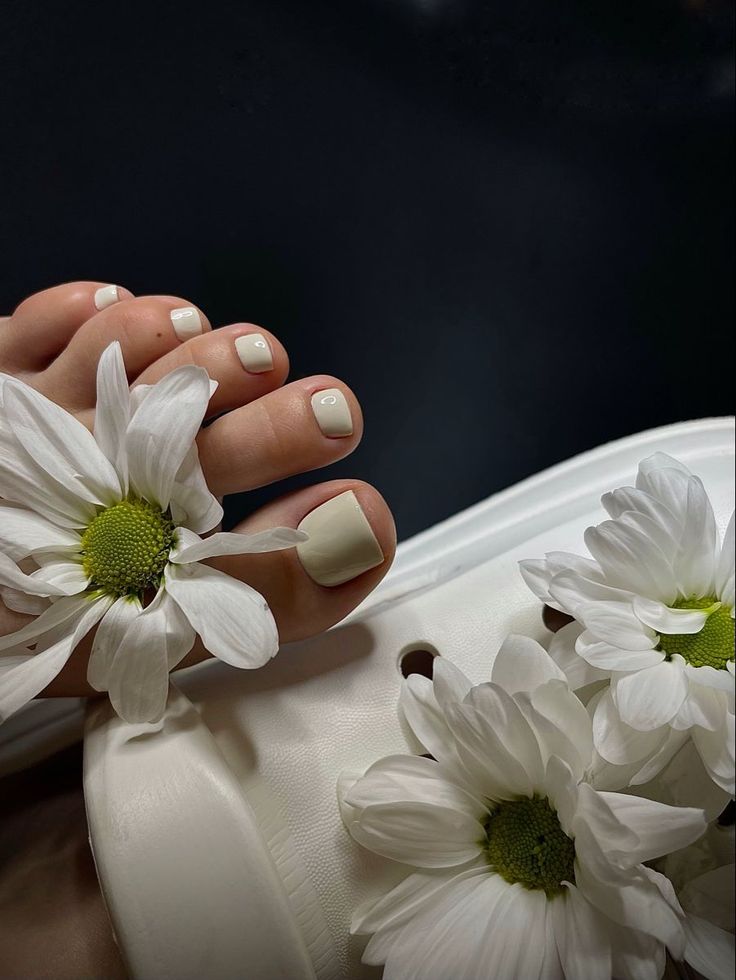 Foot with a light-colored pedicure and white daisies on a white sandal